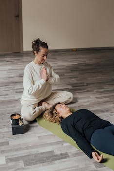 A peaceful indoor meditation session with a guide and a participant on a yoga mat.