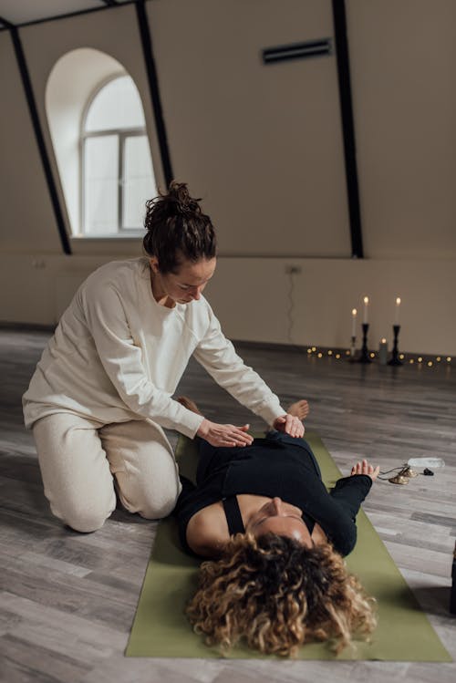Woman in White Long Sleeves Massaging a Woman Lying on a Mat