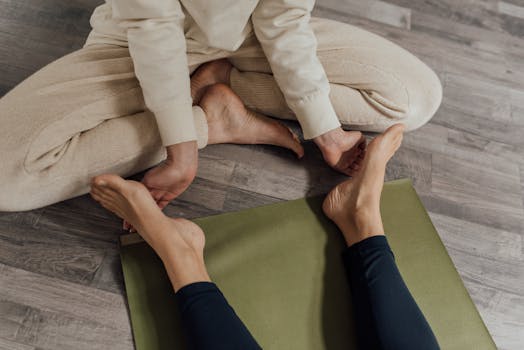 Two individuals engaged in a yoga session on a wooden floor with a green mat.