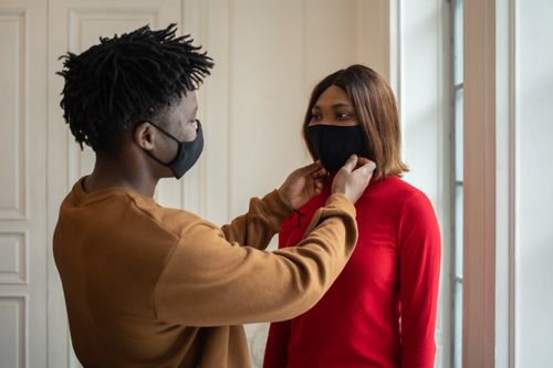 Free Caring African American male putting on medical mask on face of black woman while standing in light room during pandemic Stock Photo