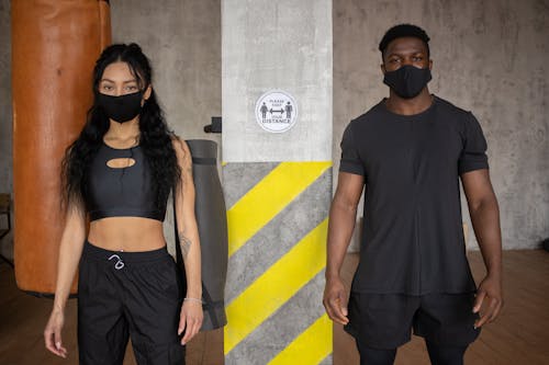 Young diverse female and African American male in protective masks standing at distance and looking at camera