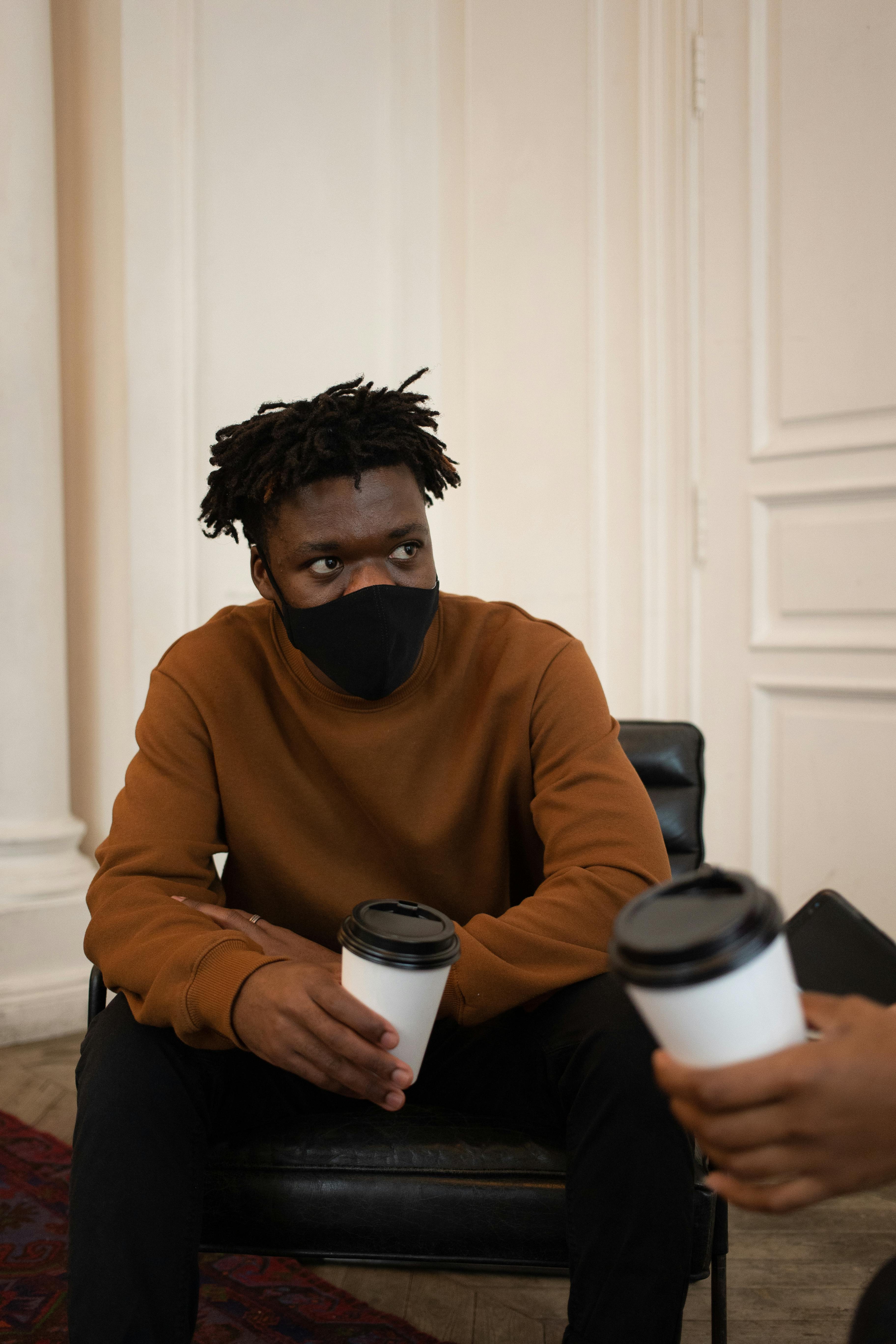 black man in protective mask with coffee talking with friend