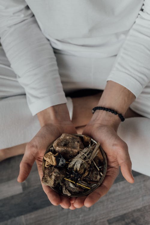 A Person Sitting Crossed Legs Holding a Bowl of Alternative Medicines