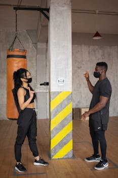 Two individuals practice social distancing and wear masks in a gym setting.