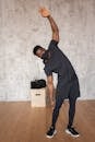 Full body of African American male in medical mask and sportswear inclining aside against wall and looking at camera