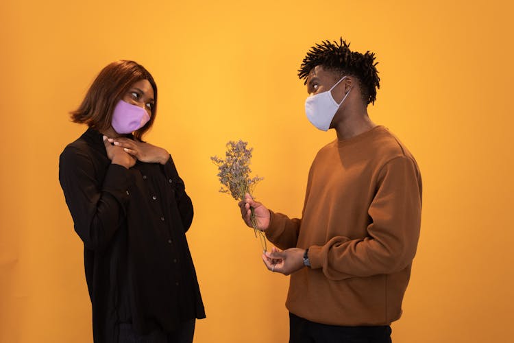 Black Man In Mask Presenting Flowers To Girlfriend In Studio