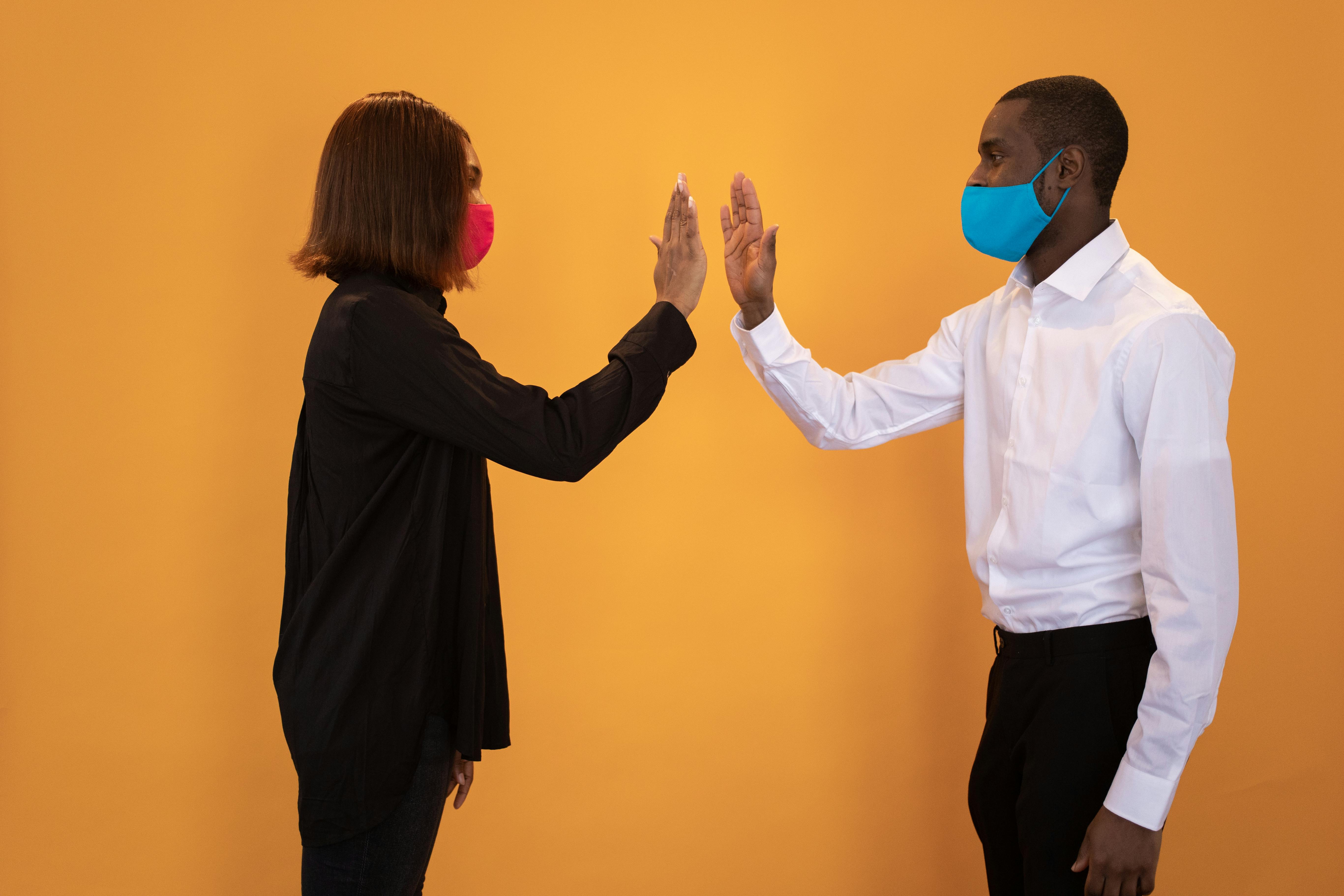 Black couple in masks giving high five in studio · Free Stock Photo