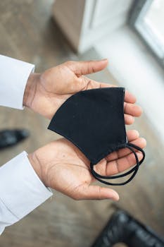 Hands holding a black face mask, symbolizing safety and protection during pandemics.