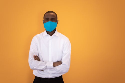 Black man in mask standing with arms folded in studio