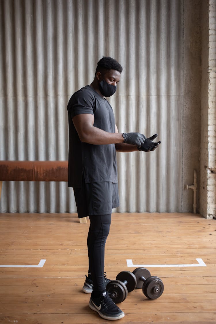 Black Sportsman In Mask Putting On Gloves In Gym