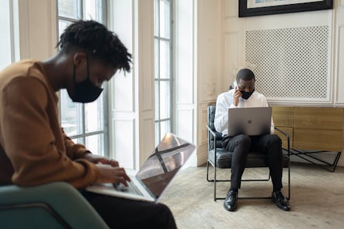 Black men in masks working on laptops in light room