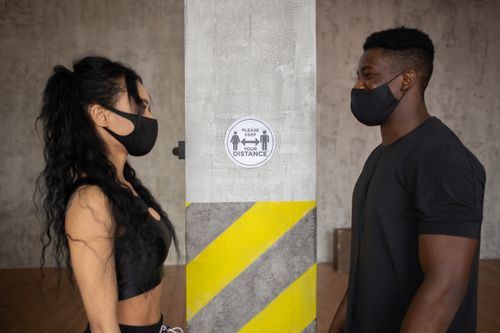 Free Side view of calm multiracial friends in protective masks standing near wall with inscription Please keep your distance Stock Photo