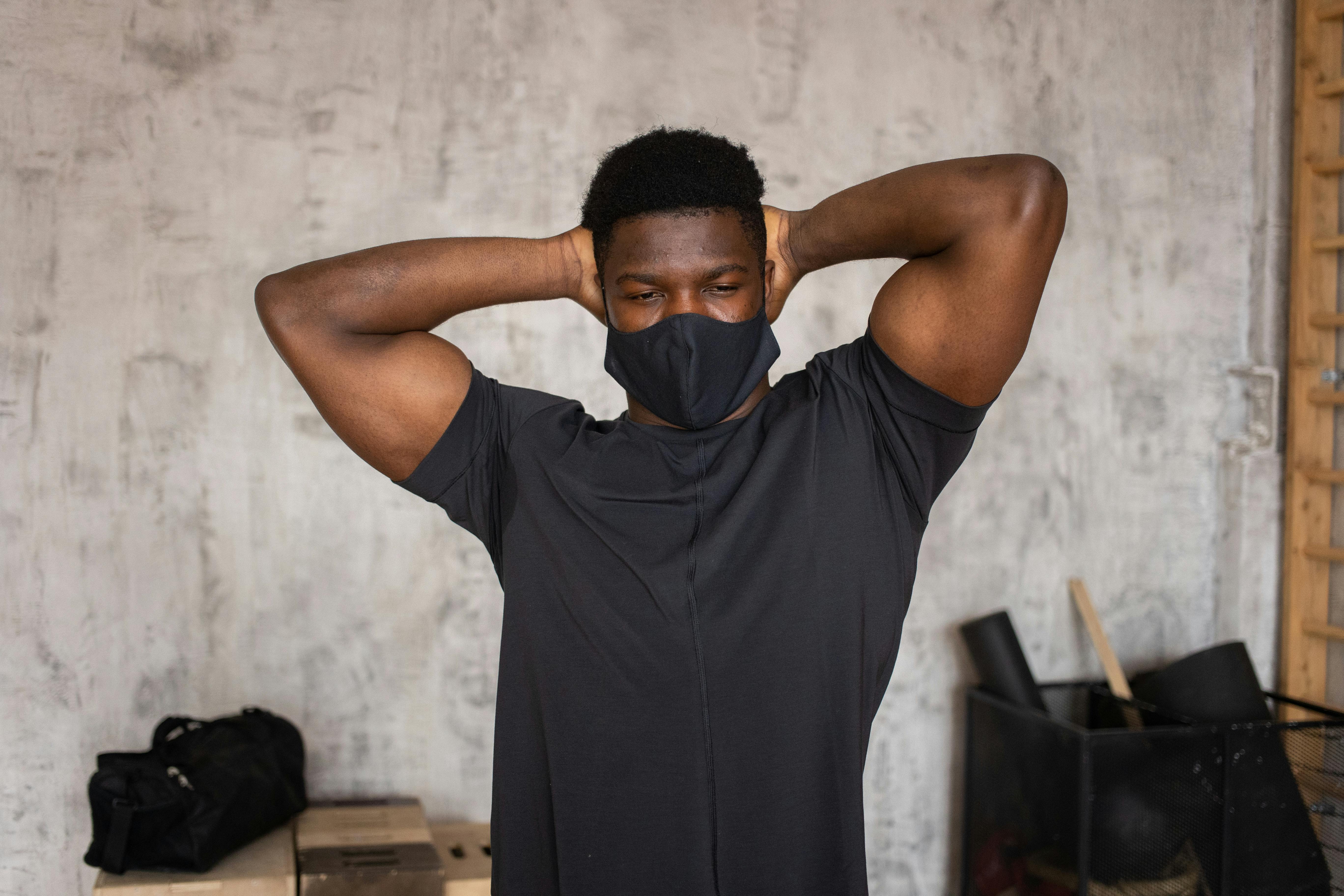 A man in activewear stands indoors wearing a face mask, looking pensive.