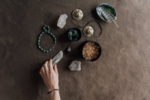 Person Holding a Drystal Beside Stones in Bowls and a String of Beads