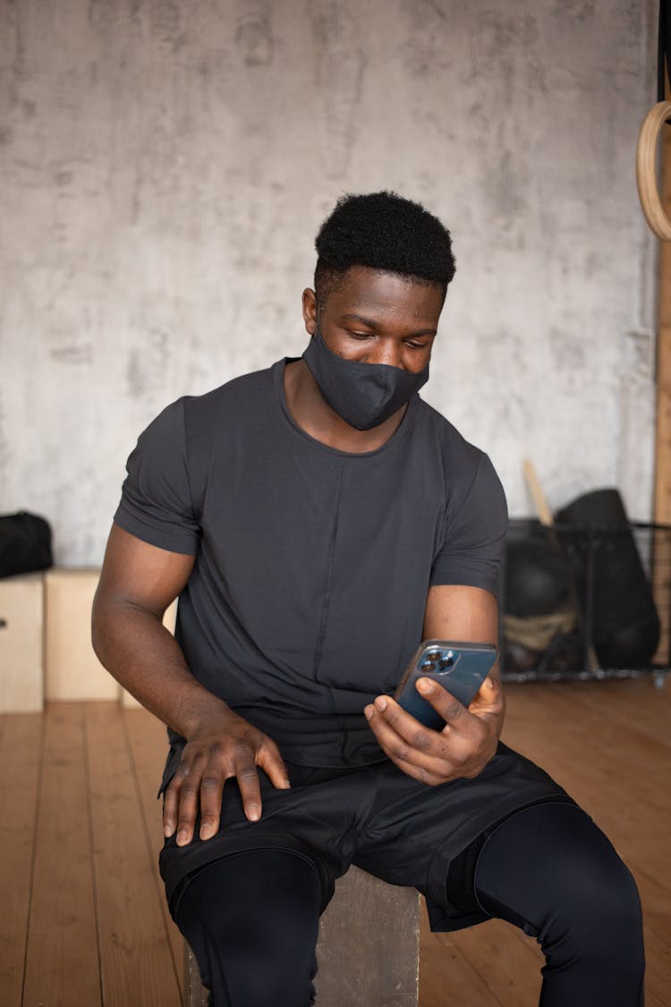 Black Sportsman In Mask Using Smartphone In Gym