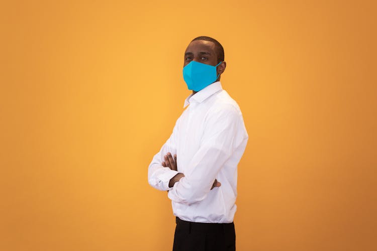 Black Man In Protective Mask Standing With Crossed Arms Against Yellow Background