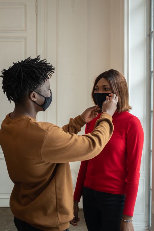 Free African American man stylish standing and putting protective mask on face of calm black woman in light room in daytime Stock Photo