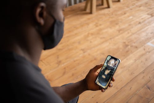 Crop black man in mask speaking with girlfriend on smartphone