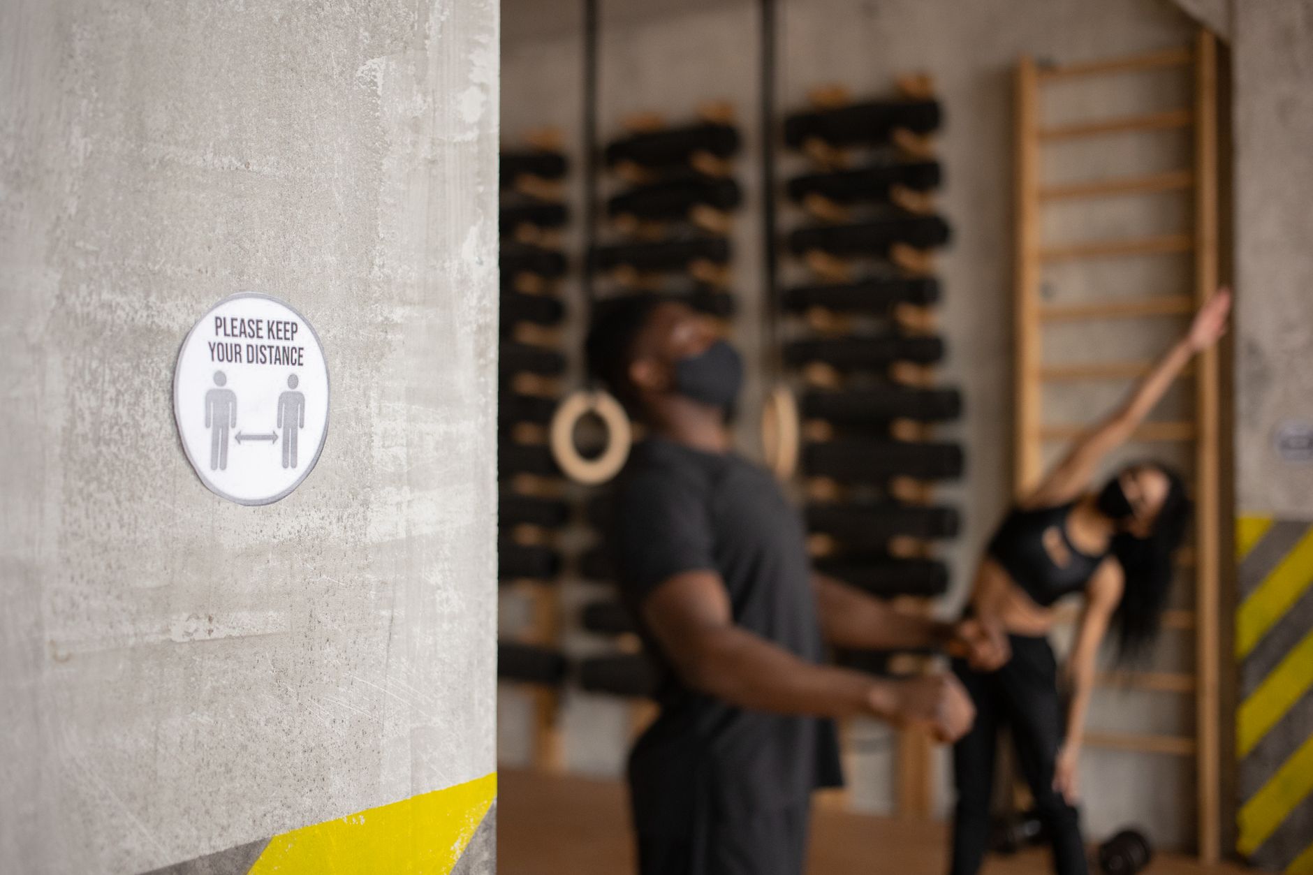 Two people exercising indoors with a social distancing sign prominently displayed.