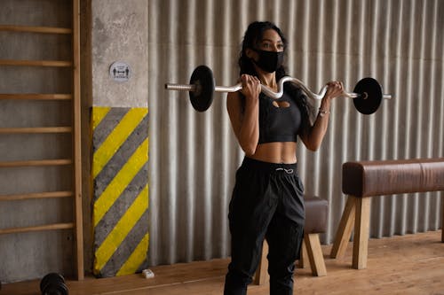 Free Black sportswoman in face mask exercising with barbell in gymnasium Stock Photo