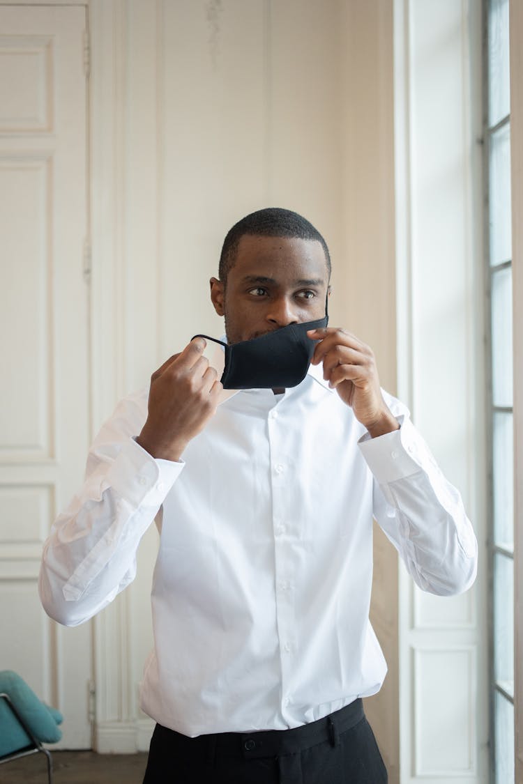 Stylish Black Businessman Taking Off Cloth Face Mask Indoors