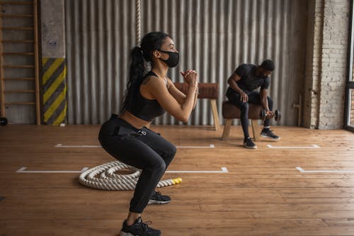 African American female athlete and unrecognizable sportsman in fabric masks exercising on floor in gymnasium