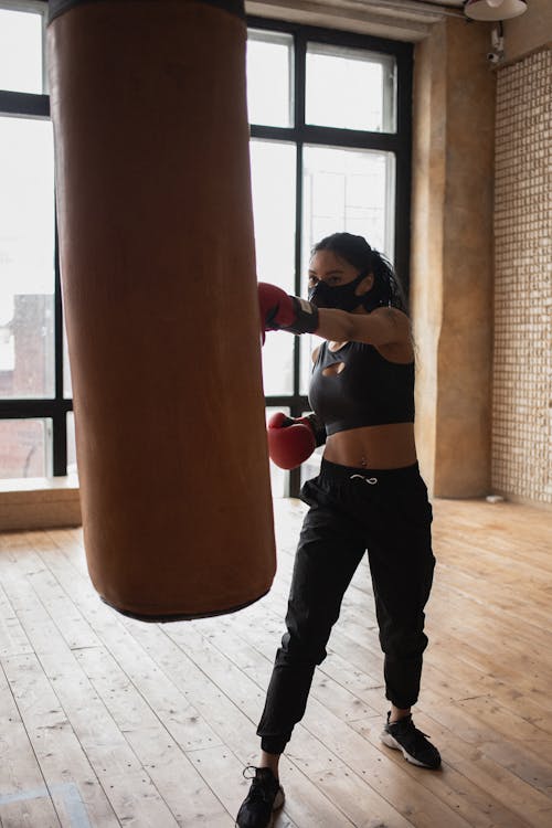 Determined black boxer hitting heavy bag during training in gymnasium
