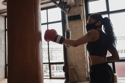 A female boxer in a gym hitting a punching bag, wearing a protective mask during practice.
