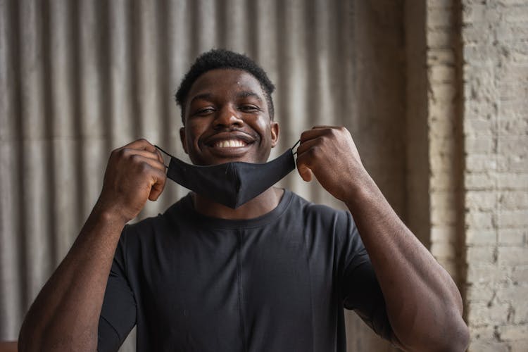 Cheerful Black Man With Fabric Mask Against Ribbed Wall