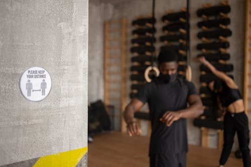 Title on sign with figures and arrows showing distance against anonymous ethnic athletes in face masks during training in gym