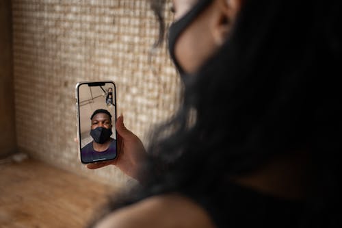 Free Back view of crop anonymous female talking to ethnic male beloved in fabric mask during video call on cellphone Stock Photo