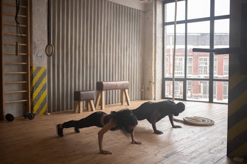 Unrecognizable black athletes in sportswear and cloth face masks standing in plank pose on floor in gym