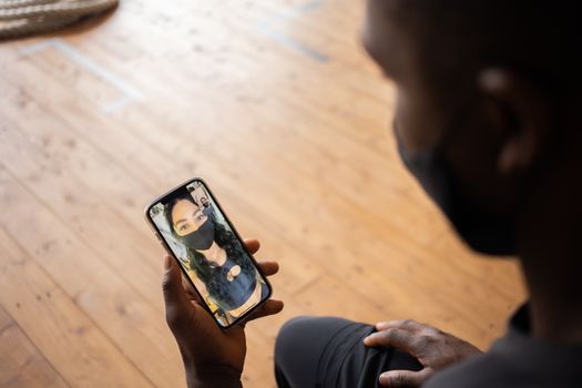 From above side view of crop anonymous ethnic male speaking with female partner on cellphone during video chat indoors