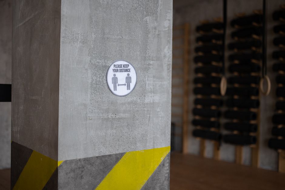 Round sign with Please Keep Your Distance title and arrow between figures on post during coronavirus pandemic in gymnasium