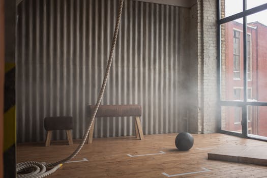 Industrial-style gym interior featuring pommel horse, exercise ball, and climbing rope.