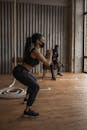 Black sportswoman squatting against partner with dumbbell in gymnasium