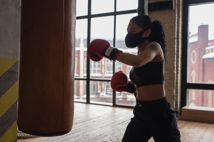 Black Boxer In Textile Mask During Training Against Heavy Bag