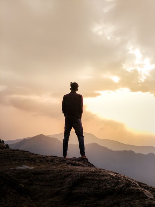 Free A man stands silhouetted against a sunset sky atop a mountain, embodying adventure and success. Stock Photo