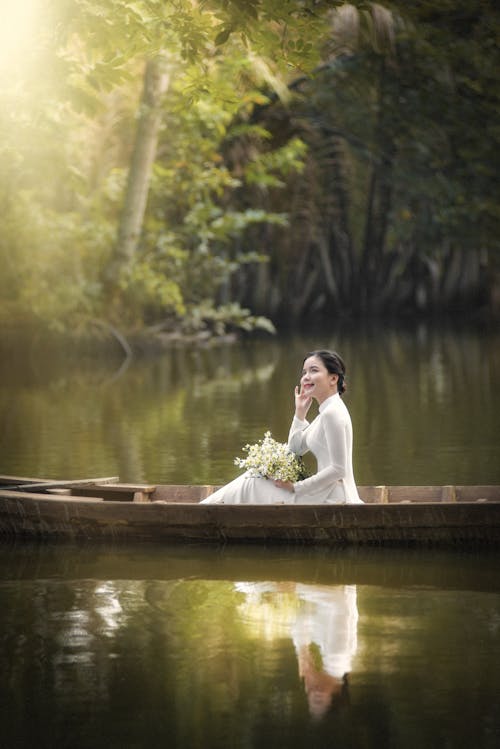 Woman in White Dress Sitting on Brown Wooden Canoe