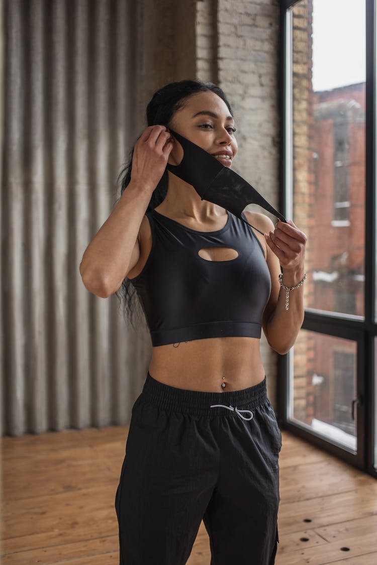 Smiling Black Sportswoman Putting On Fabric Mask In Gym