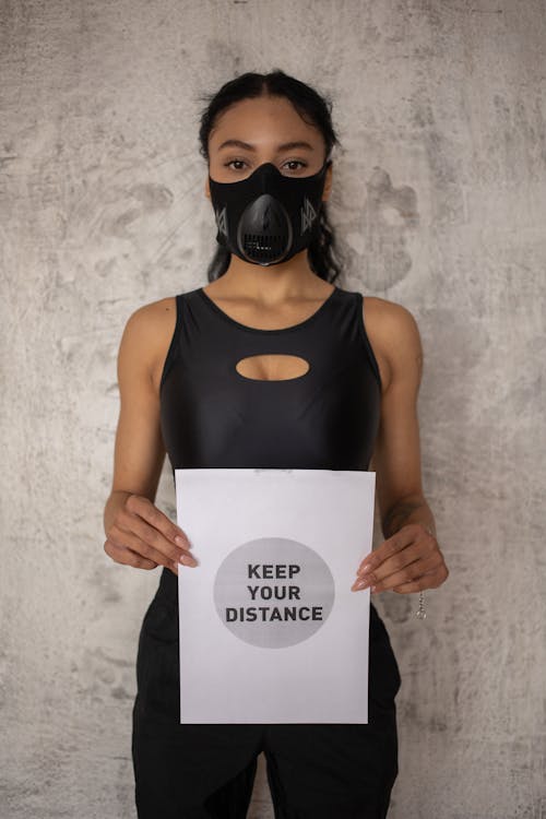 Black woman in respiratory mask showing inscription on paper
