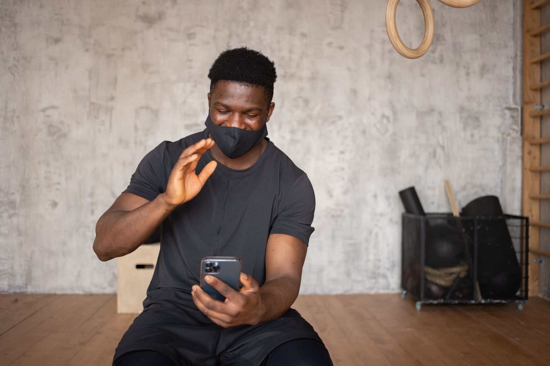 Smiling man with face mask using smartphone for video call indoors. Waving and communicating online.