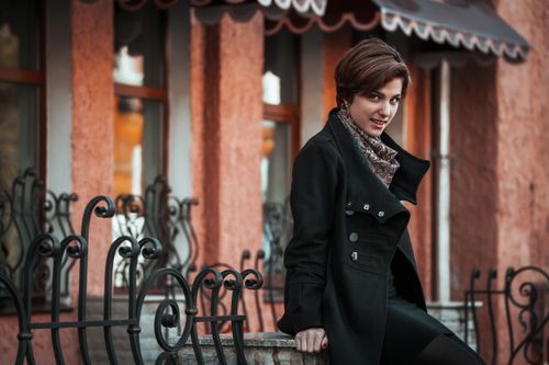 Free Stylish woman sitting on a city railing, showcasing modern fashion in a serene urban setting. Stock Photo