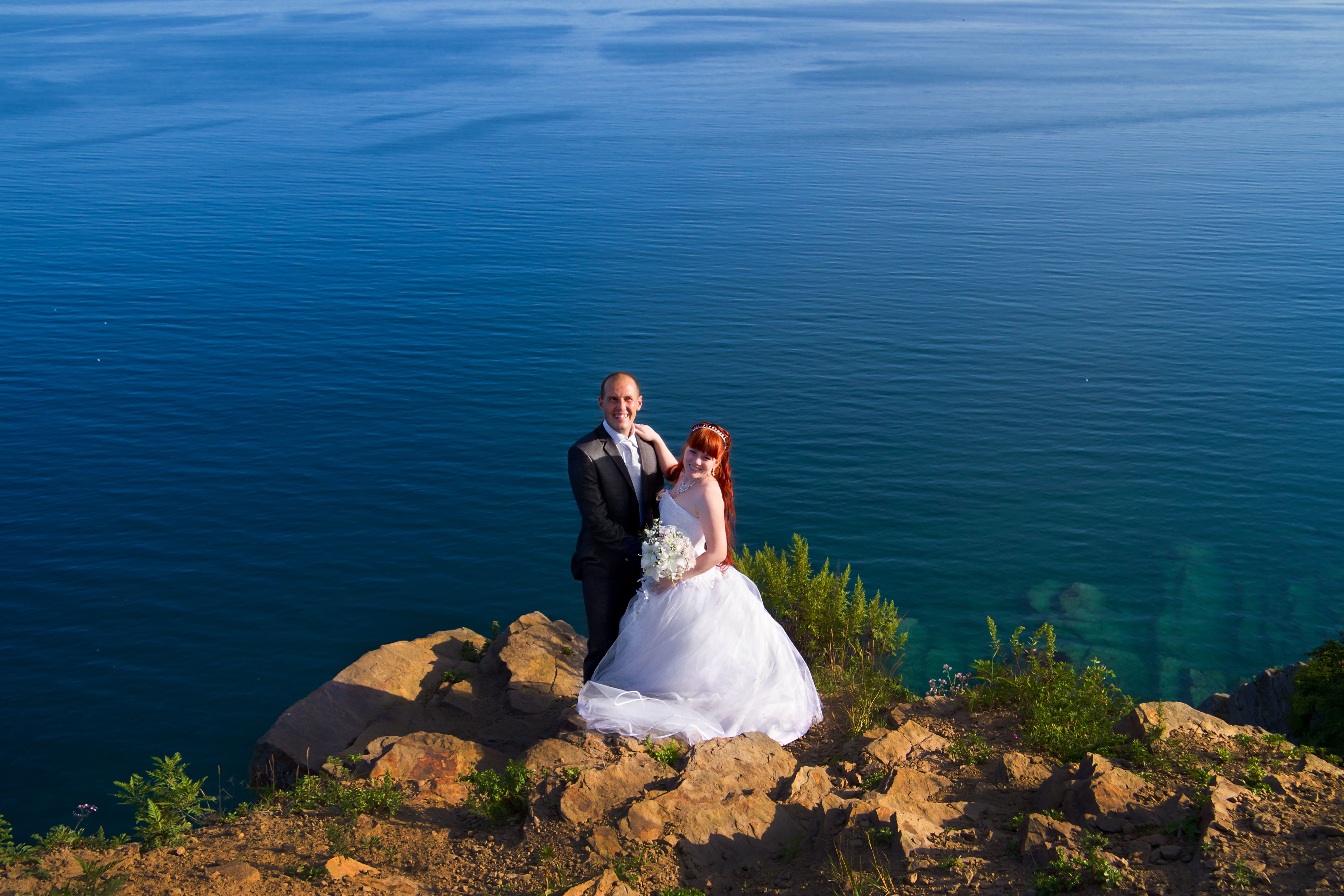 Elegant wedding couple stands on a cliff with serene ocean views, embracing nature and romance.