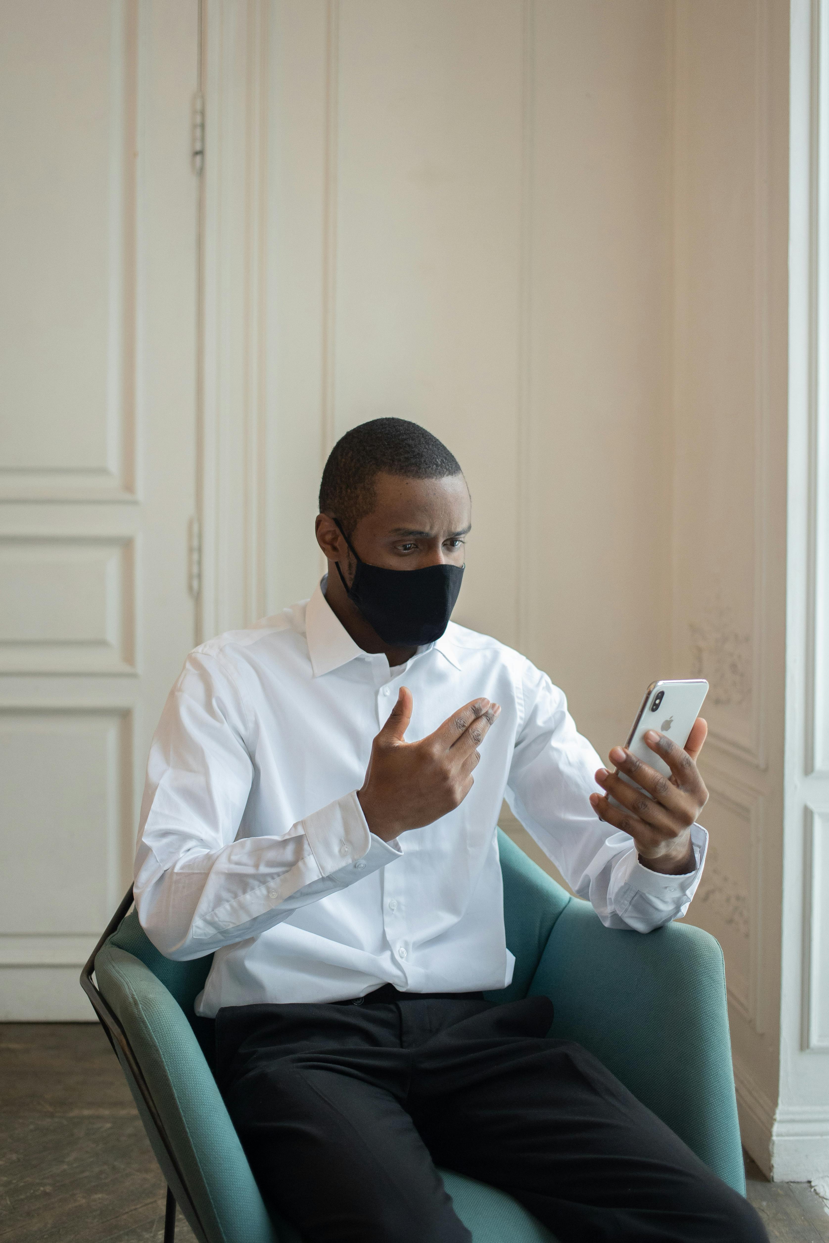 serious black businessman gesticulating while speaking on smartphone indoors