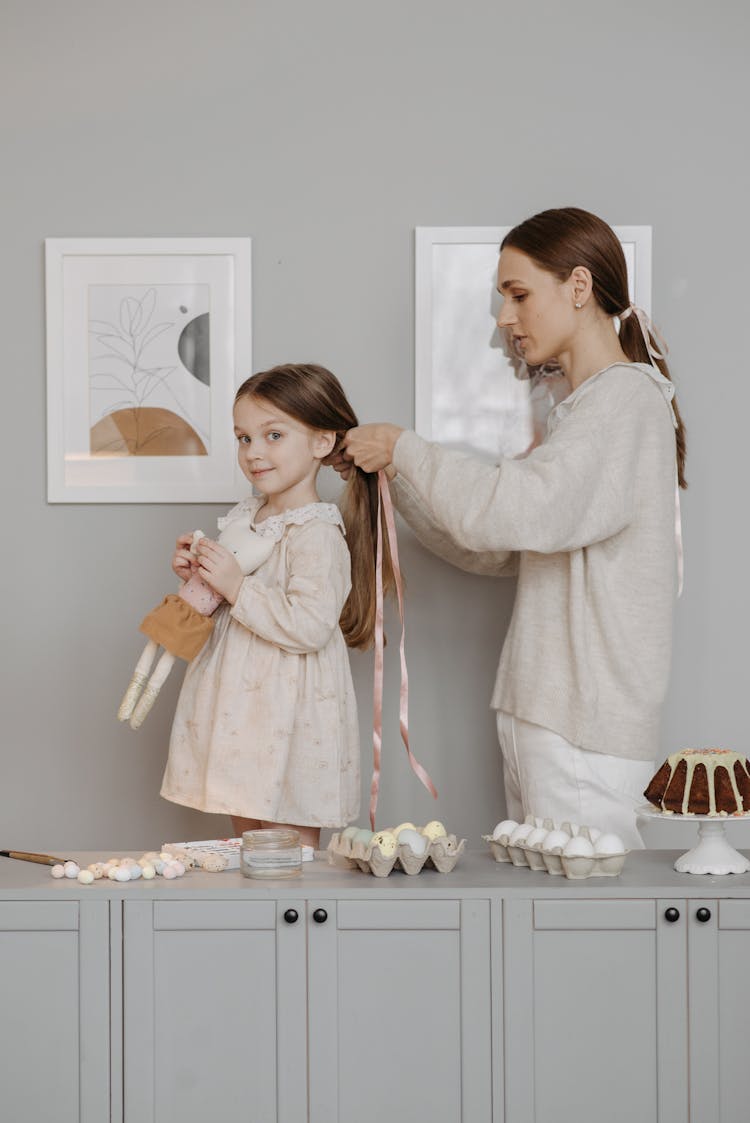 A Mother Tying Her Daughter's Hair With A Ribbon