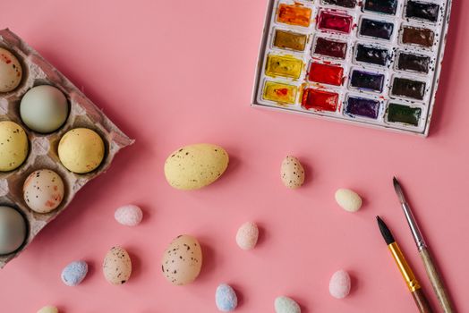 Decorative Easter eggs with watercolor palette and brushes on pink background for festive arts and crafts.
