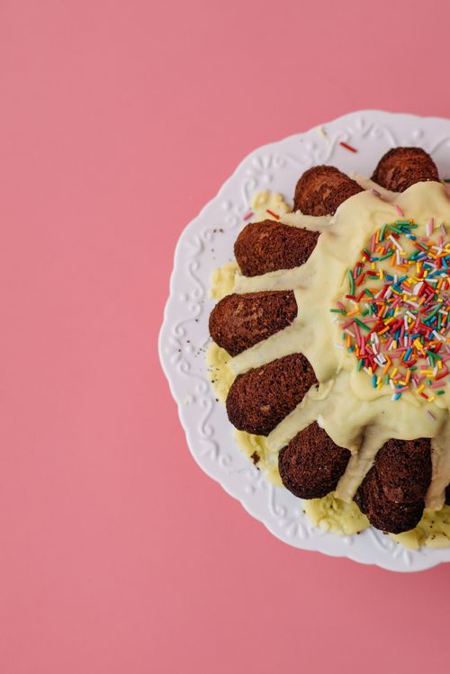 Free Close-up of a bundt cake with frosting and sprinkles on a pink surface. Stock Photo