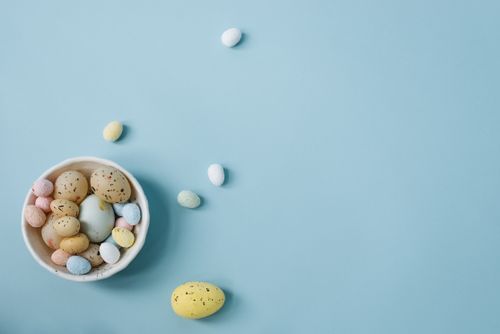 Free Vibrant Easter eggs in a bowl on a pastel blue background, perfect for seasonal themes. Stock Photo