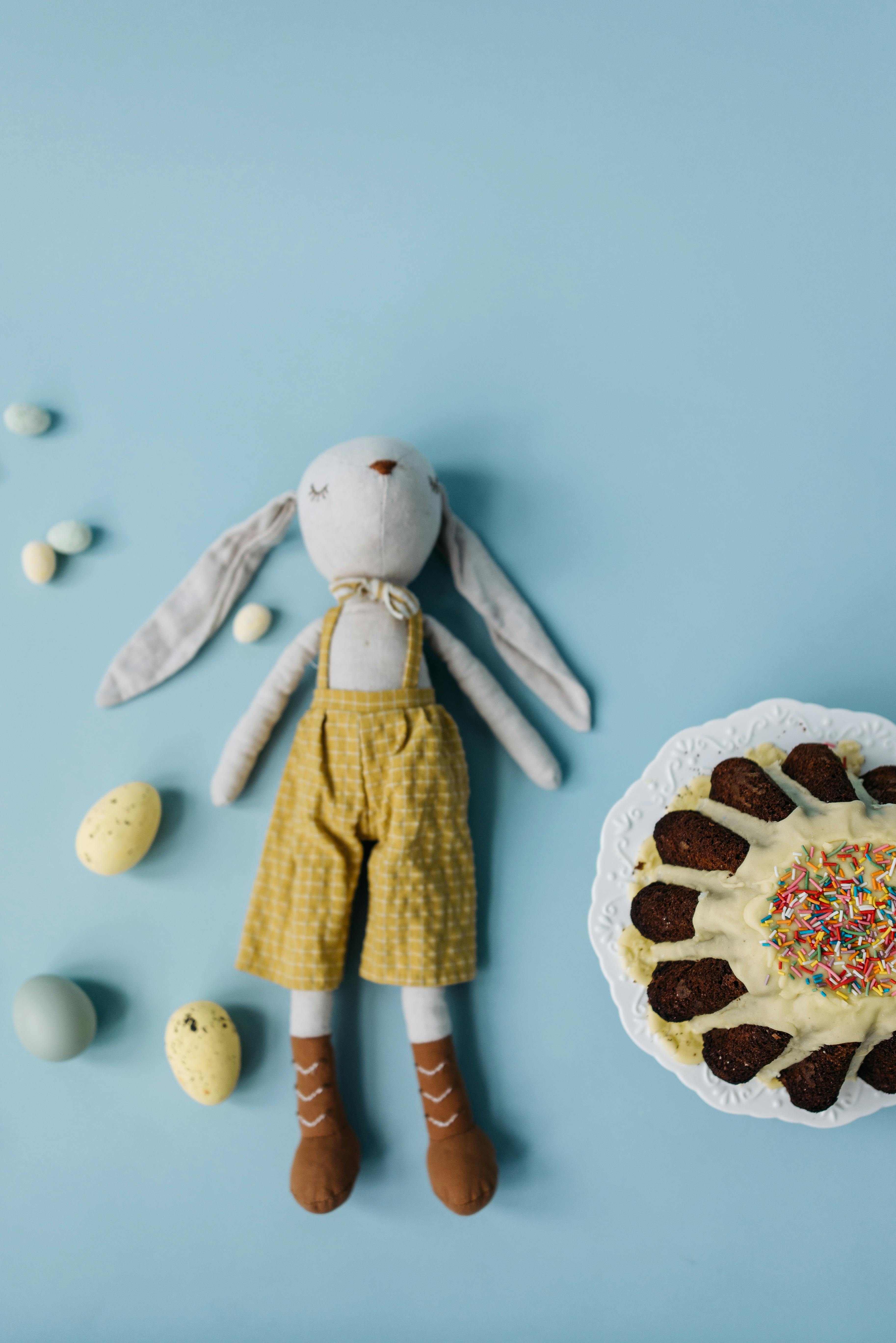 bunny stuffed toy with eggs and sprinkle cake on light blue blackground